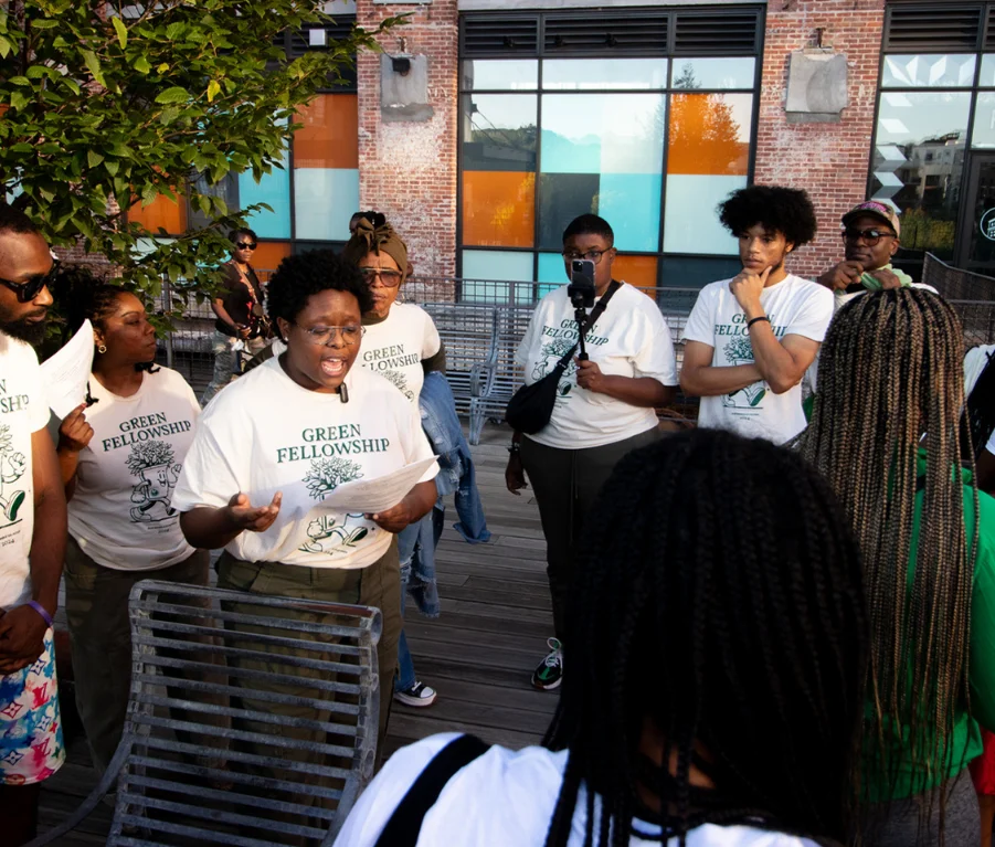 Group of Sustainable Georgia Futures volunteers speaking to crowd all wearing "green fellowship" tshirts on a patio at Ponce City Market in Atlanta, Georgia