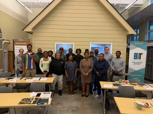 Group photo of workshop participants standing in front of a 'Diagnostic Cabin' training model, in a classroom set up with tables and a 'Better Buildings BIT' banner.