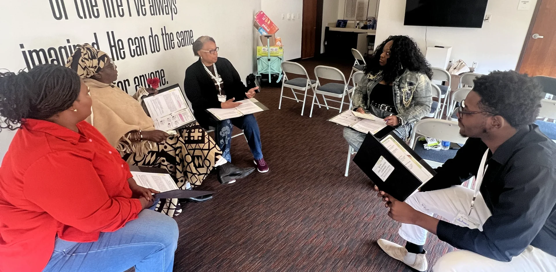 Group sitting in a circle of chairs holding folders of information and discussing