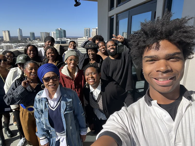 Team group selfie taken on an outdoor rooftop balcony with a city skyline in the background, everyone smiling and posing together.