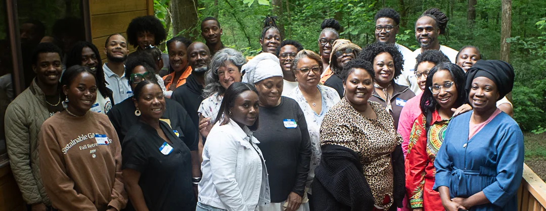 Group photo of about a dozen smiling people of varying ages standing and posed on a deck in front of a wooded area