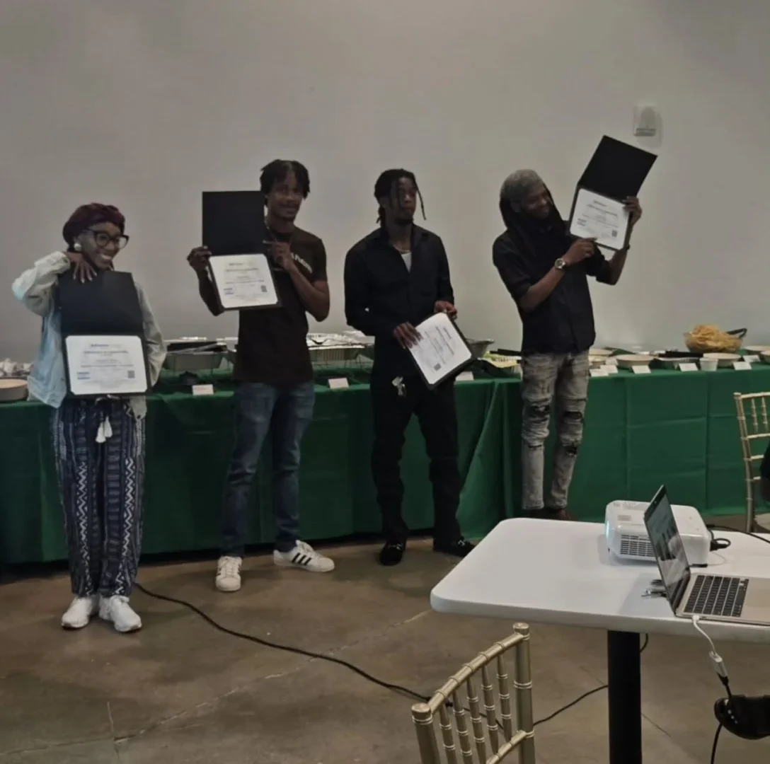 4 graduates of the solar and weatherization pre-apprenticeship holding up their diplomas in front of a buffet table of food at graduation reception